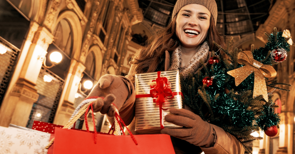 Woman smiling, holding holiday shopping bag.
